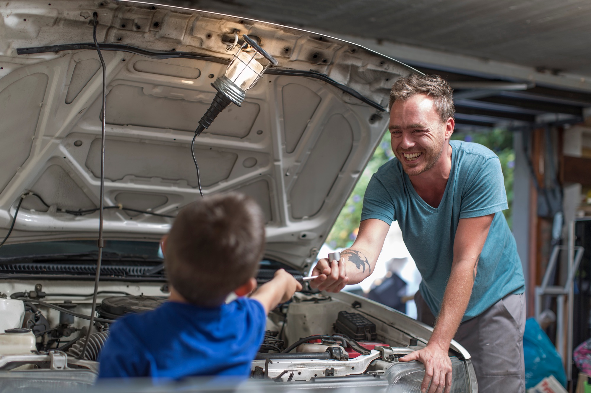 Son helping father in home garage working on car