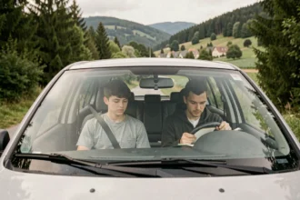 Vue d'ensemble d'un élève en auto-école dans les Vosges, assis avec son moniteur dans une voiture de conduite sur une route bordée de forêts