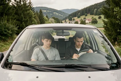 Vue d'ensemble d'un élève en auto-école dans les Vosges, assis avec son moniteur dans une voiture de conduite sur une route bordée de forêts